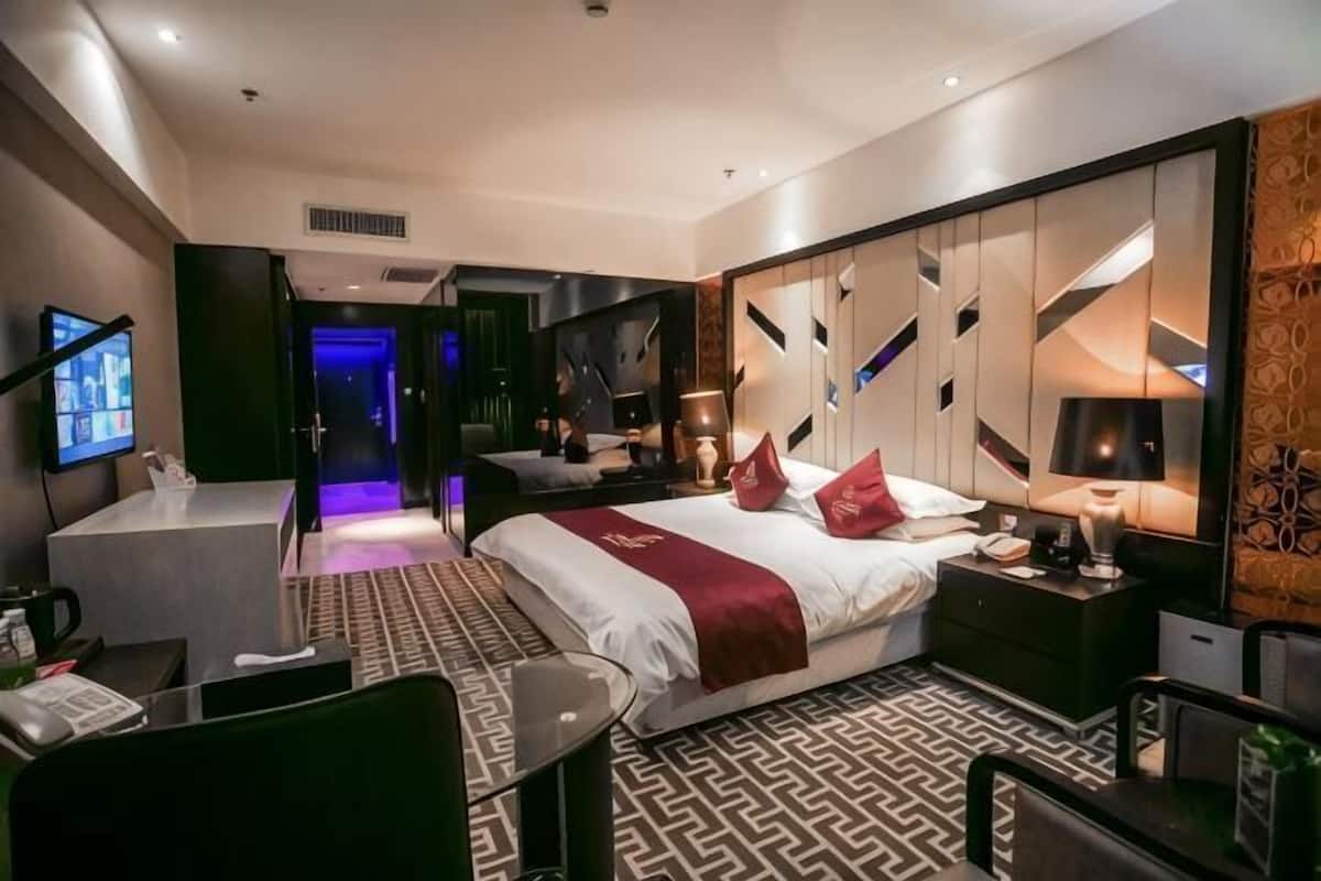 Ein modernes Hotelzimmer mit Bett, Nachttisch, Fernseher und Schreibtisch mit Stuhl.