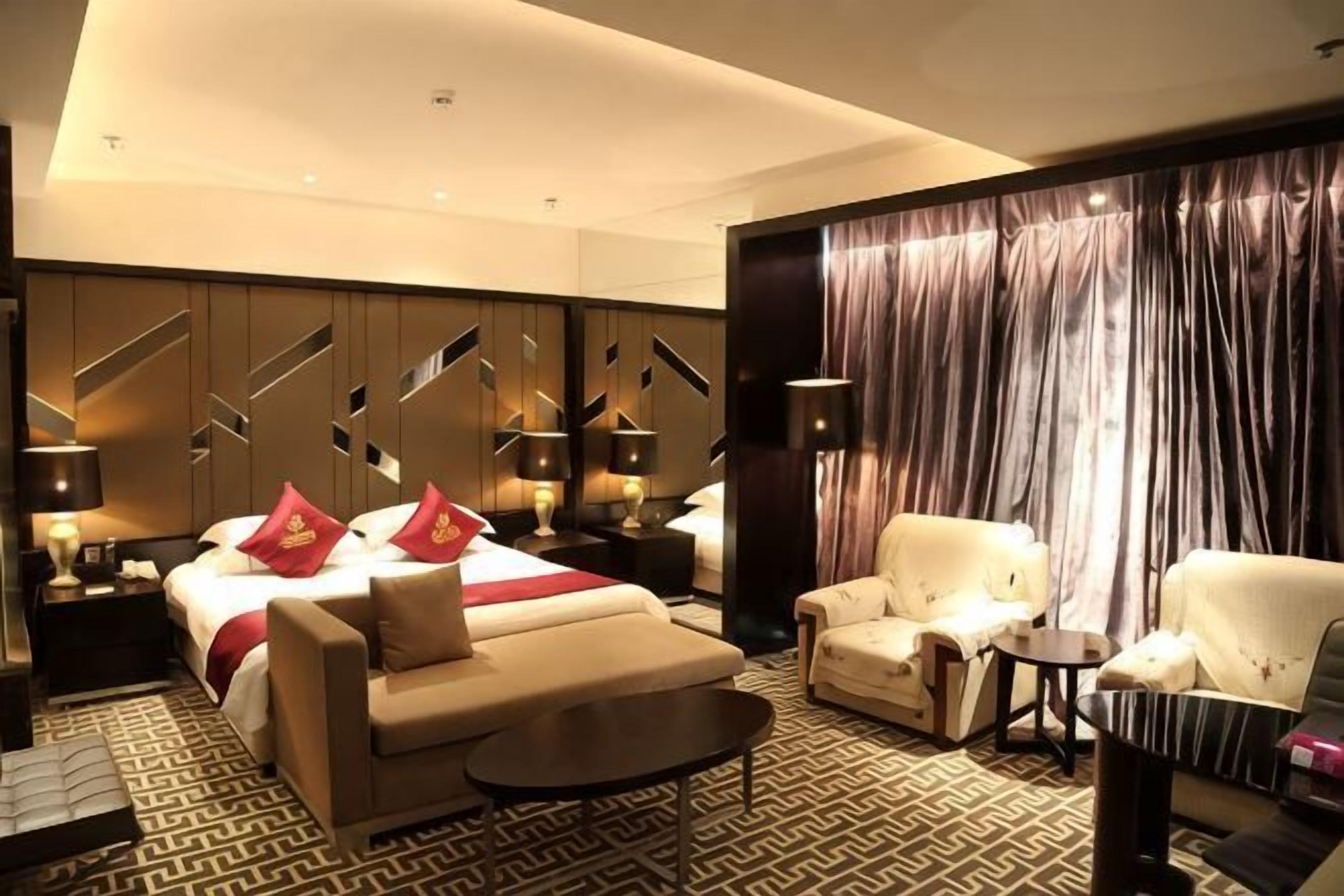 A hotel room with a bed, a sofa, a chair, a small table, and a large window with curtains.