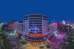 Un edificio de varios pisos con fachada curva, señalización iluminada y un estacionamiento al frente.