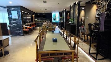 Un restaurante con una larga mesa y sillas, un pilar de mármol y una pared negra con una planta.