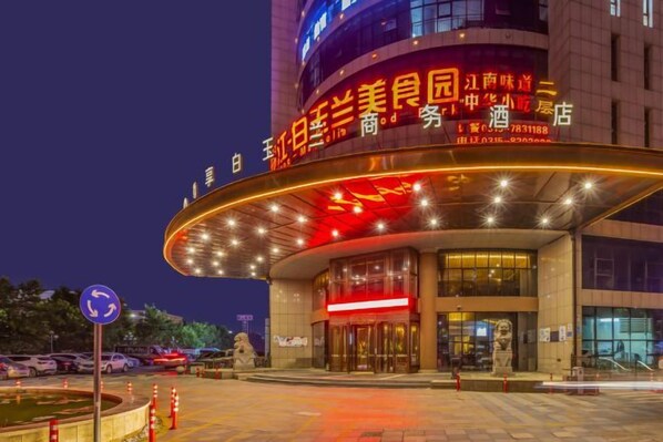 A hotel with a curved entrance, illuminated signage, and a parking area. - Tangshan Magnolia Business Hotel (Convention Center University Road) (Tangshan)