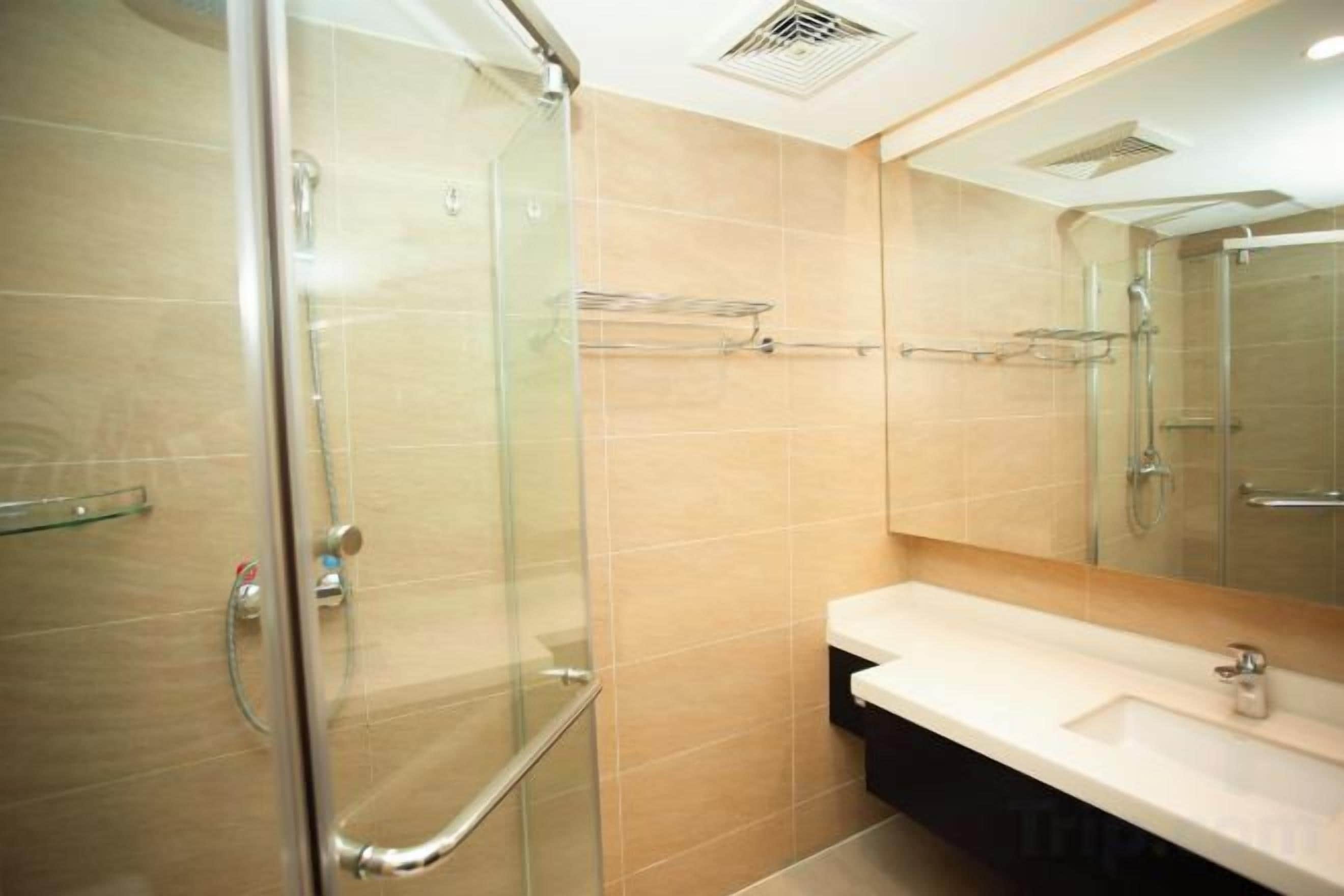 Ein modernes Badezimmer mit Duschkabine aus Glas, Waschbecken mit Spiegel und beige gefliesten Wänden.