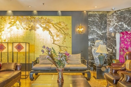 A modern living room with a sofa, armchairs, a coffee table, and decorative elements like a vase with flowers and wall art.