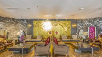 A spacious lobby with a marble floor, a central seating area with sofas and armchairs, and a decorative wall with a golden mural.