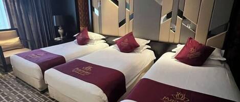 Hotellihuoneessa on kolme sänkyä, joissa kaikissa on valkoinen patja ja tummanpunainen pääty. Huoneessa on kuvioitu matto ja suuri peili seinällä.