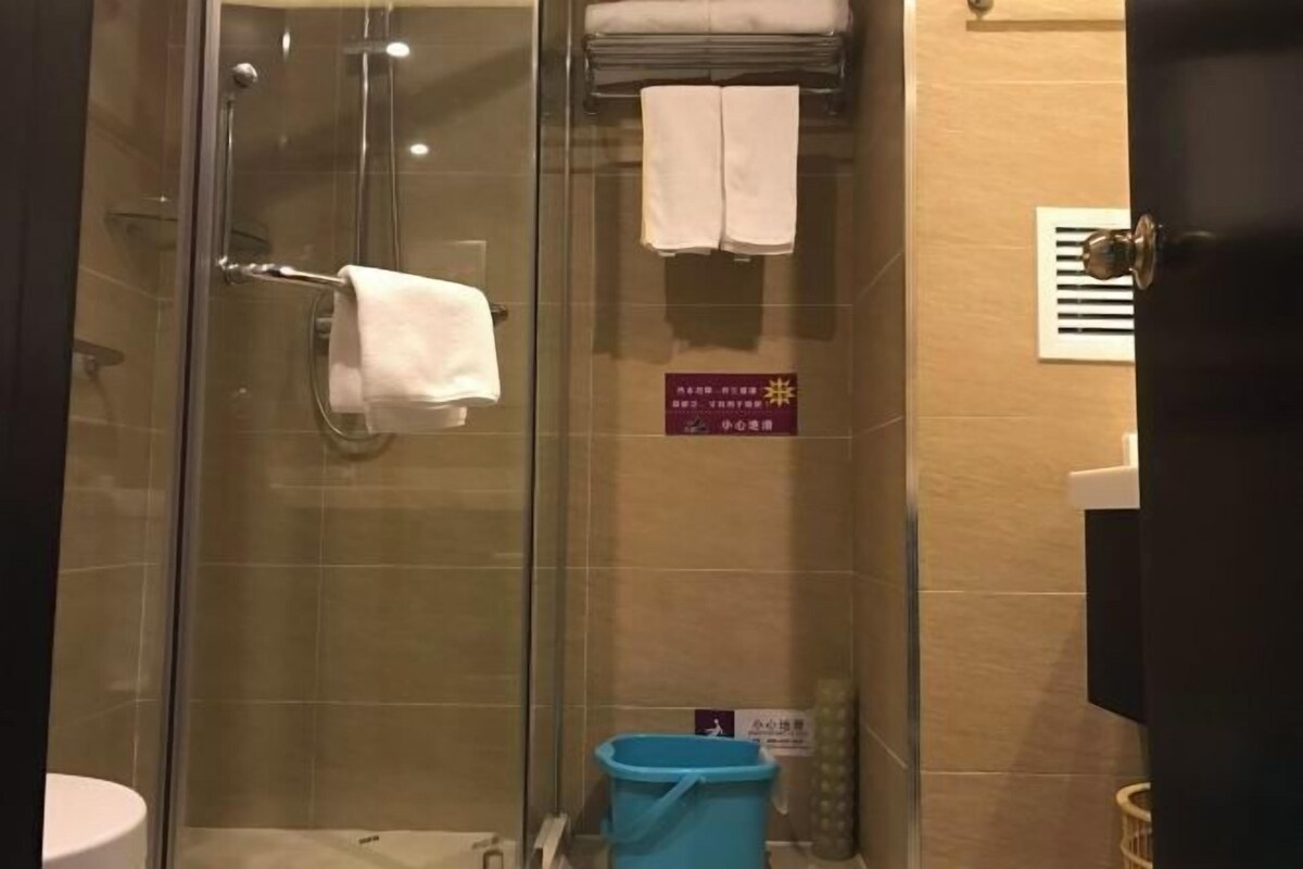 A glass-enclosed shower area with a towel rack and a blue trash bin.