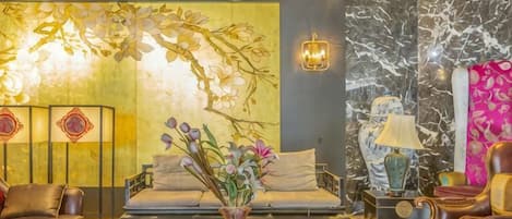 Een moderne zithoek met een bank, fauteuils, een salontafel en decoratieve elementen zoals een vaas met bloemen en wanddecoratie.