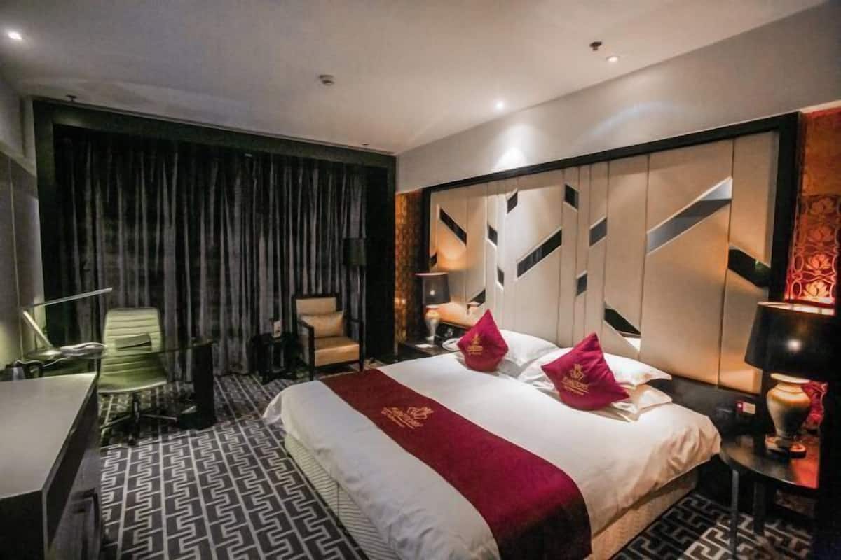 A hotel room with a large bed, a desk, a chair, a desk lamp, and a wall with geometric patterns.
