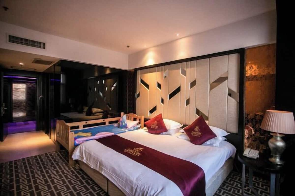 A hotel room with a bed, a desk, a lamp, and a patterned floor.