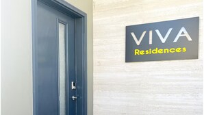 Una puerta azul con placa metálica protectora y un escalón pequeño que lleva a ella. Un cartel sobre la puerta dice "VIVA Residences".