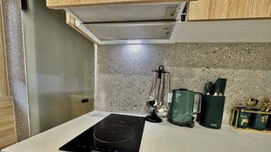 Een keuken met een zwart inductiekookveld, een groene waterkoker en een lepelrek.