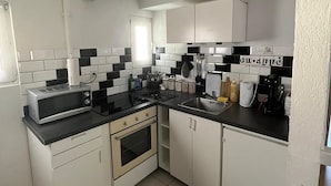 Una cocina compacta con armarios blancos, una encimera negra y un microondas.