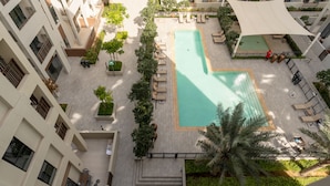An aerial view of a hotel courtyard with a swimming pool, lounge chairs, and palm trees. - Serene Hideaway w Top Facilities in Creek Beach (Dubai)