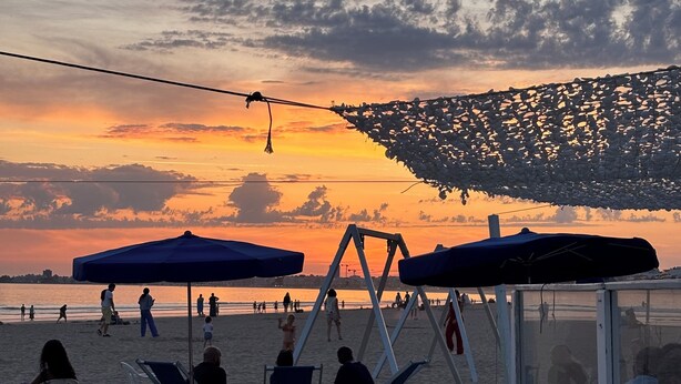 Una platja amb seients ganduls blancs i ombrel·les, un tobogan i vistes a la posta de sol sobre l'oceà.