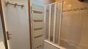 Un bany amb una porta blanca, un penjador de tovalloles, una dutxa amb porta de vidre i un tapet de bany verd.