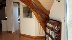 Una habitació àmplia amb un sostre alt, bigues de fusta a la vista, una prestatgeria integrada i una finestra gran.