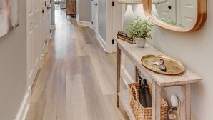 A hallway with a wooden floor, a mirror, a lamp, and a console table with baskets.