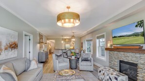 A spacious living room with a stone fireplace, grey sofas, and a large TV mounted above it.