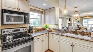 A kitchen with white cabinetry, a black stove, a granite countertop, and a hanging light fixture.
