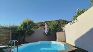 A swimming pool with a ladder, surrounded by a wooden fence, palm trees, and a view of a hill. - Luxury villa (Armissan)