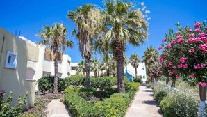 A pathway lined with palm trees and flowering plants, leading to a building with a white facade and blue accents. - Muses Hotel (Rhodes)
