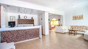 A reception area with a brick counter, a wooden bookshelf, a clock, and a sofa with a floral pattern. - Muses Hotel (Rhodes)