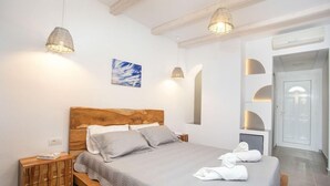 A bedroom with a wooden headboard, a bed with grey bedding, two bedside lamps, a nightstand, and a painting on the wall. - Muses Hotel (Rhodes)