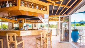 A bar area with wooden furniture, shelves with bottles, and a glass door leading outside. - Muses Hotel (Rhodes)