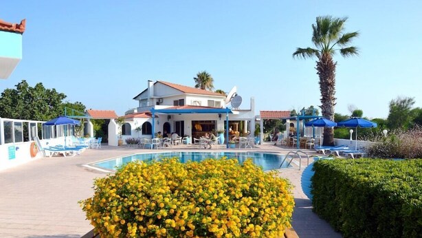 A pool area with lounge chairs, a building with a red roof, and a palm tree. - Muses Hotel (Rhodes)