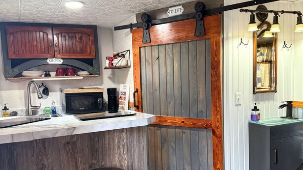 A kitchen with a wooden bar, two stools, a microwave, and a coffee maker.