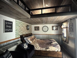 Un dormitorio con techo de madera, pared de piedra, cama con ropa de cama estampada, un reloj y una cita motivacional en la pared.