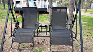 A swing set with two chairs and a small table in a wooded area.