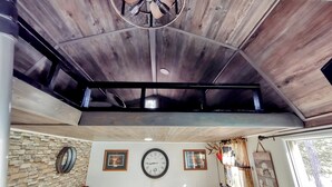 A room with a wooden ceiling, a clock on the wall, and a stone wall.