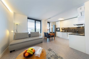Un appartement moderne comprenant un canapé, une table à manger, un coin cuisine et un panier de fruits posé sur une table basse.