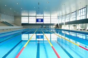 Une piscine intérieure avec des couloirs bien délimités, un plafond haut et de grandes fenêtres.