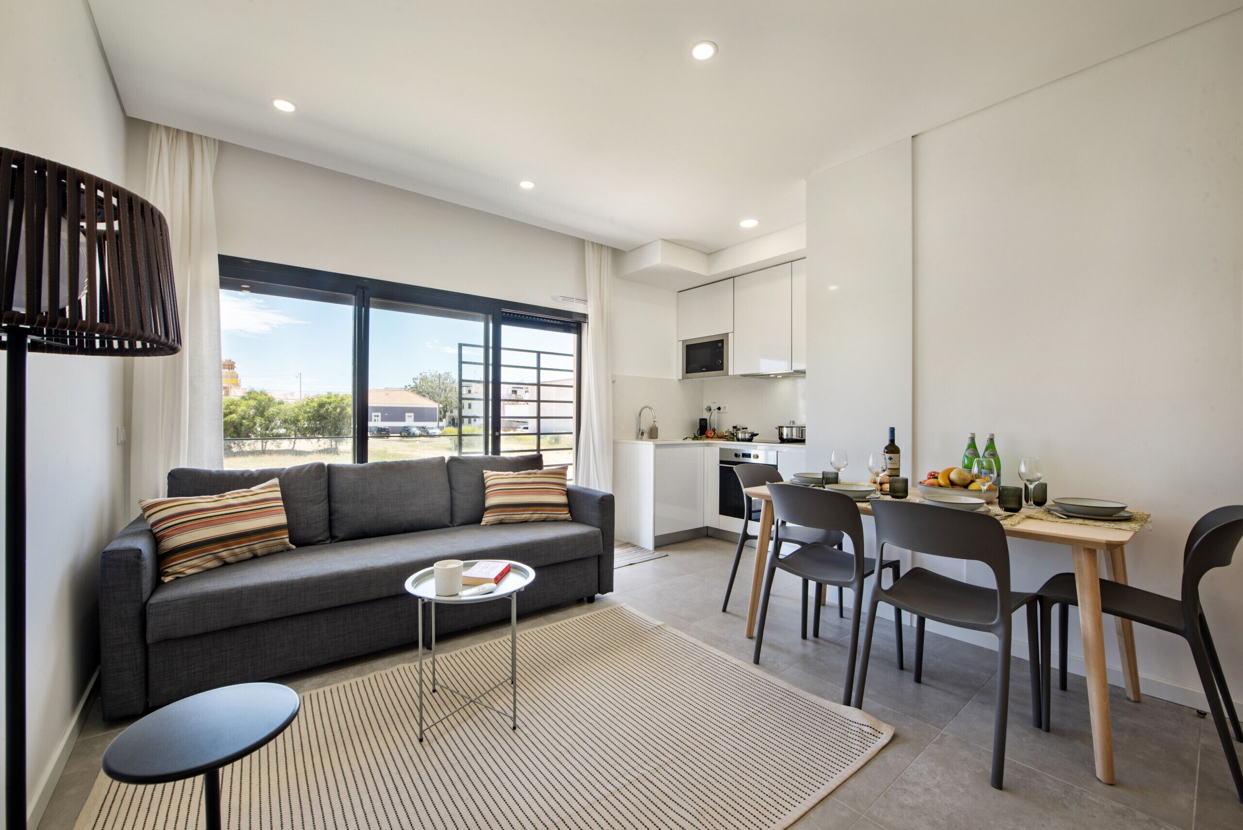 A modern living room with a sofa, a small round table, and a dining area with chairs and a table set for two.