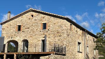 Un edificio de piedra con un balcón, arcos de entrada y una chimenea.