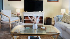 A living room with a television, two framed artworks, a white cabinet, wicker furniture, and a glass coffee table.
