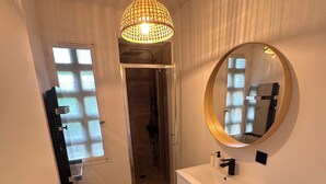 Un bany modern amb un penjador blanc, un mirall rodó, zona de dutxa i lluminària al sostre.