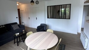 Un saló modern amb una taula rodona de fusta, dues cadires, un sofà i una finestra gran amb cortines.