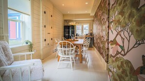 A dining area with a wooden table and chairs, a window with blinds, and a wall with a tree mural. - Mallard Inn (St. John's)