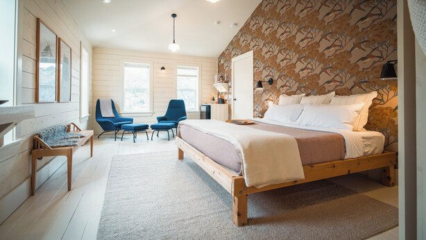 A bedroom with a large bed, two chairs, a desk, and a window. - Mallard Inn (St. John's)