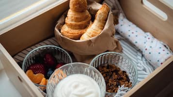 Une boîte en bois contenant des pâtisseries, du yaourt et un mélange de fruits secs et de granola.