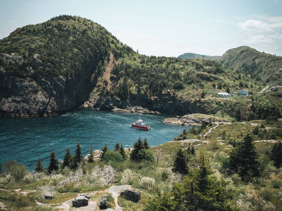 A coastal landscape with a boat on the water, surrounded by hills and greenery.