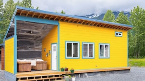 Keltainen mökki, jossa on kuisti, puiset penkit ja ruukuissa olevia kasveja.