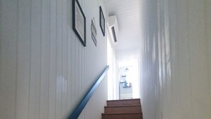 Un escalier en bois, avec des murs blancs et une rampe bleue, mène à une pièce lumineuse située à l’étage.