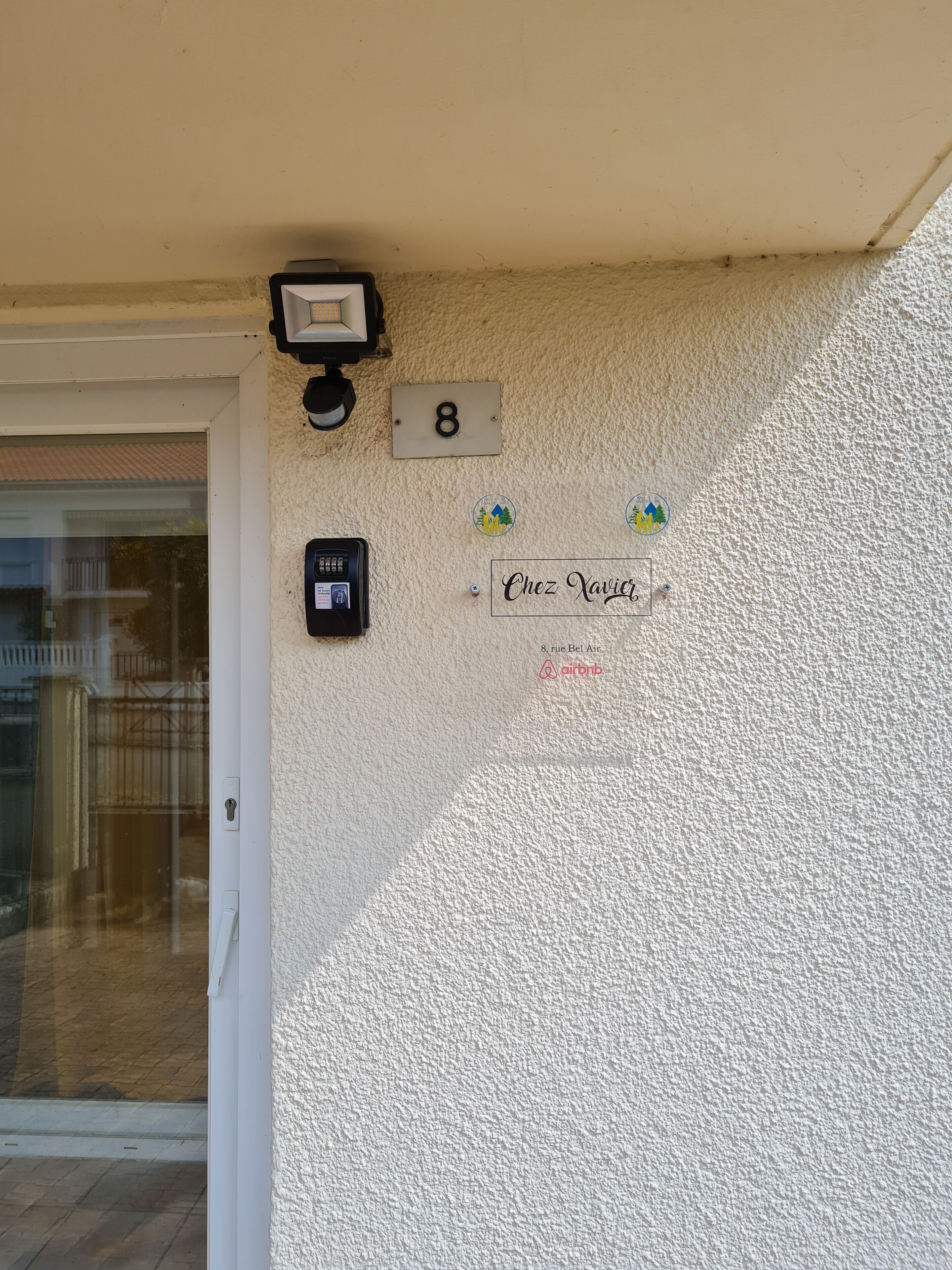 A textured wall with a house number '8', a security camera, a doorbell, and a sign reading 'Chez Xavier'.