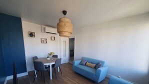 Un salon moderne avec un canapé bleu, une table à manger avec des chaises, un luminaire suspendu et une porte donnant sur une autre pièce.