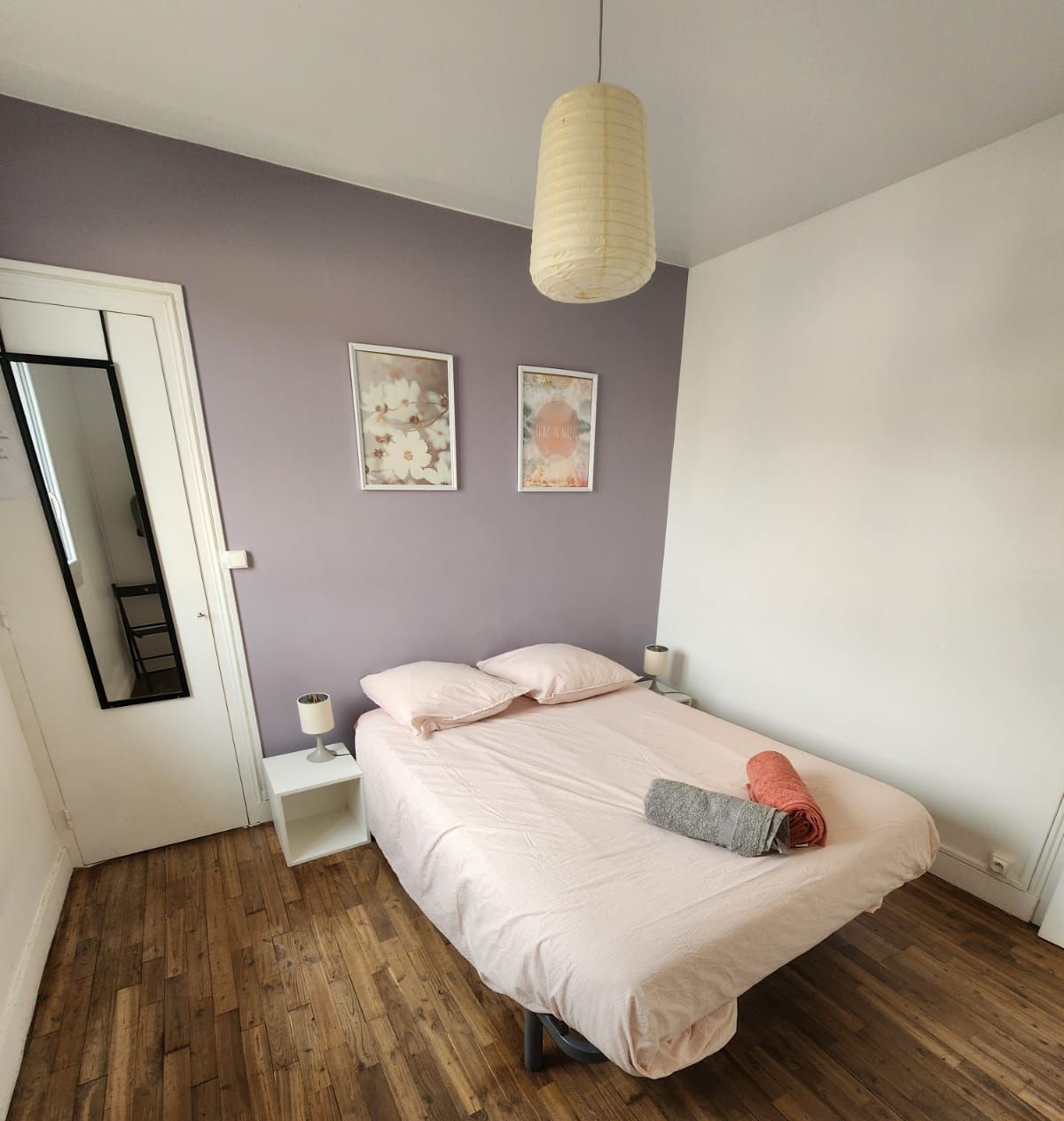 A bedroom with a bed, a nightstand, a lamp, and a hanging light fixture.