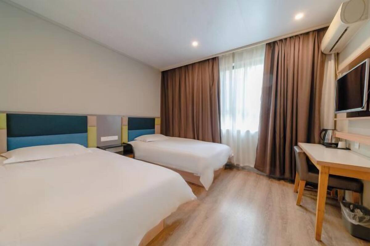 Ein Hotelzimmer mit zwei Betten, einem Schreibtisch, einem Sessel, einem Fernseher und einer Klimaanlage.